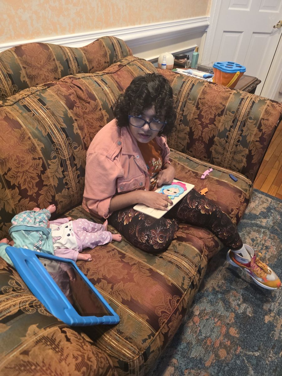 Bethany on the couch at home with a puzzle, her doll and her iPad