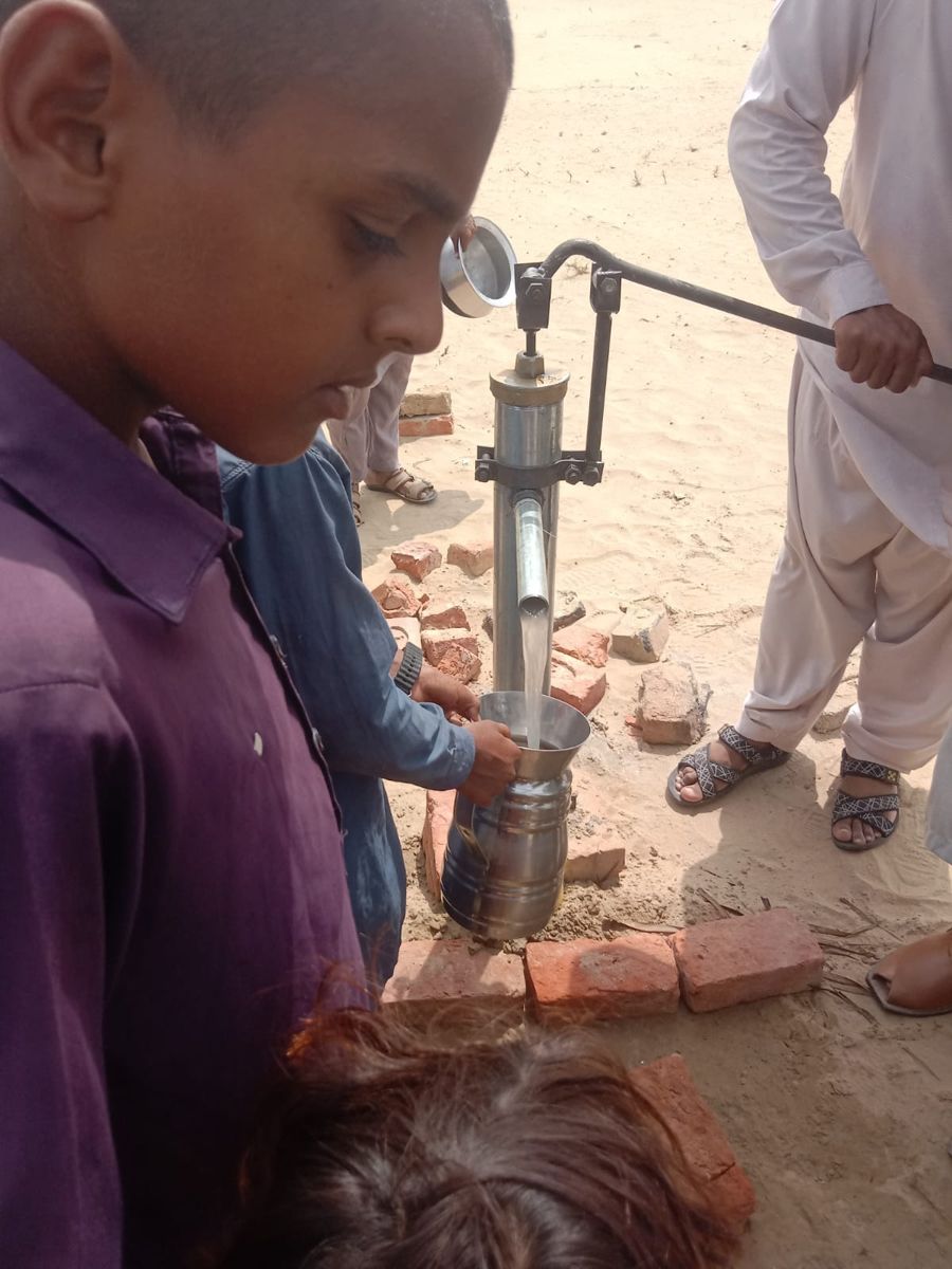 Children filling a steel jug with clean water from a hand pump